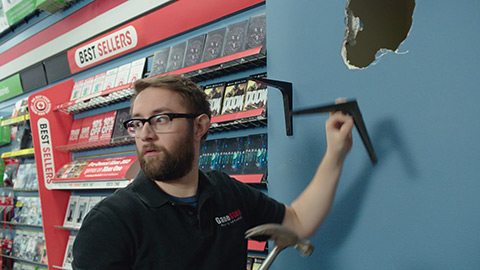 Man holding shelf bracket near hole in the wall