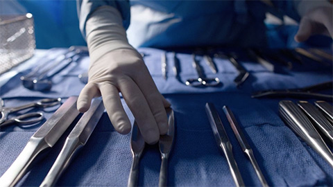 gloved hand positioning a tray of surgical instruments
