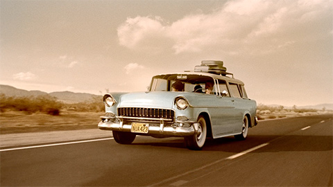 Vintage station wagon with luggage on top cruising down the road