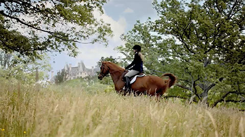 Woman riding a horse with Biltmore Estate in the distance