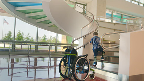 Boy climbing up stairs with wheelchair at bottom of stairs