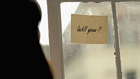 Woman looking at Will you? sign taped to window