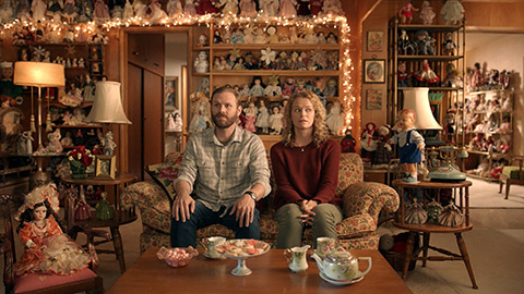 Man and woman sitting on couch in room full of dolls