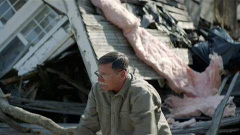 Man sitting in front of a destroyed house