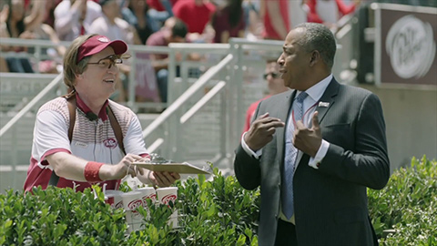 Larry Culpepper dressed in Dr Pepper gear talking to man in suit at football game