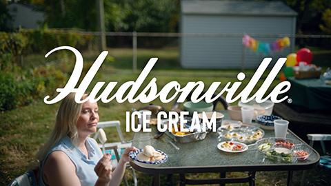 Woman eating ice cream at table set for a party with Hudsonville Ice Cream superimposed over the image