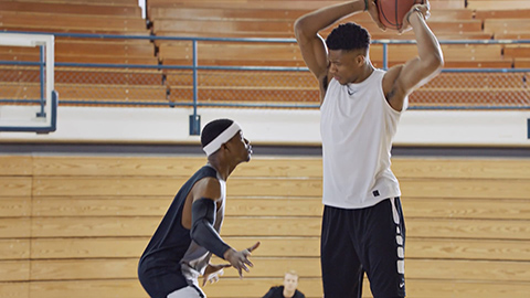 2 men playing basketball, one is really tall holding ball up